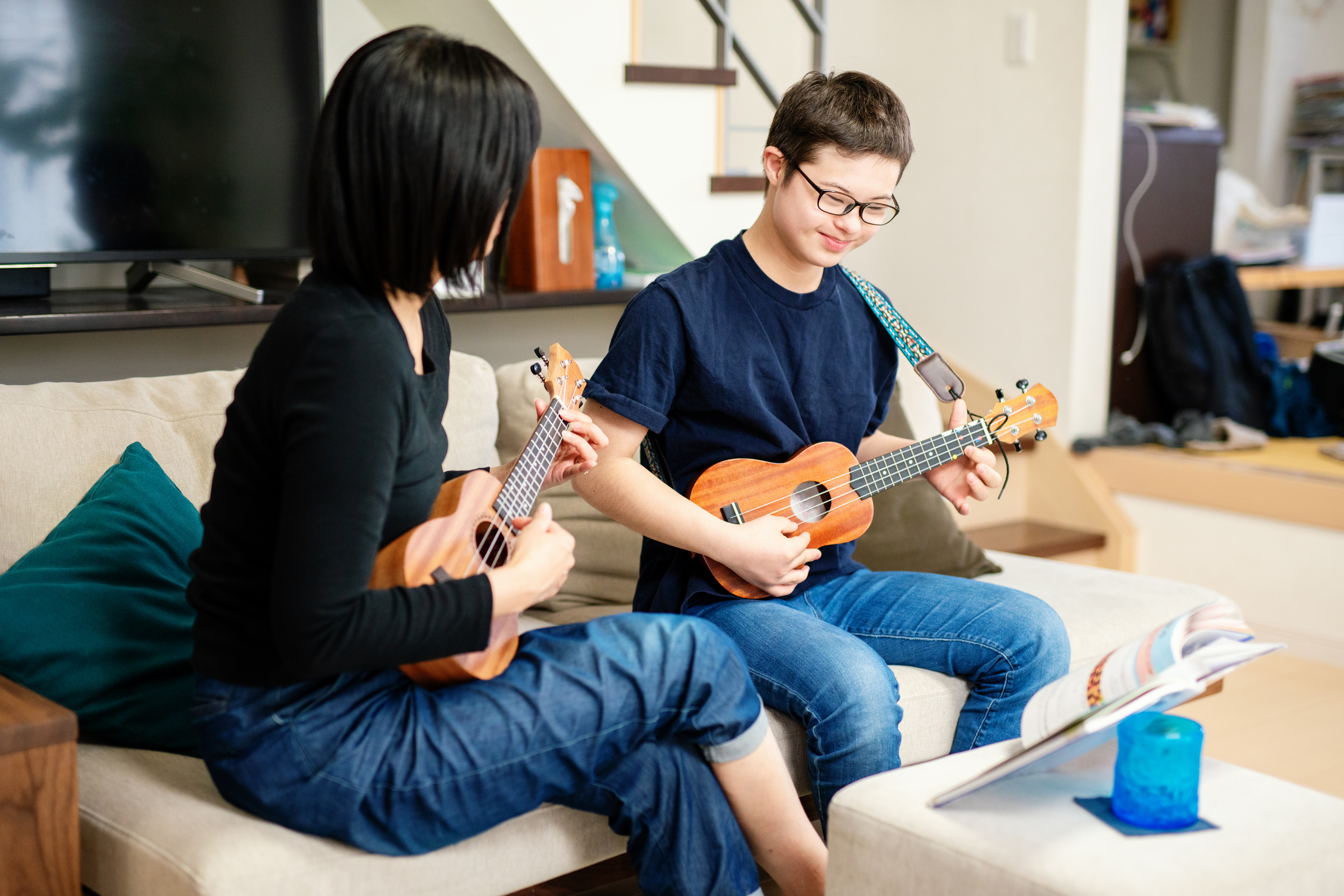 Teenage boy with Down's Syndrome practicing ukelele with his mother at home in Japan