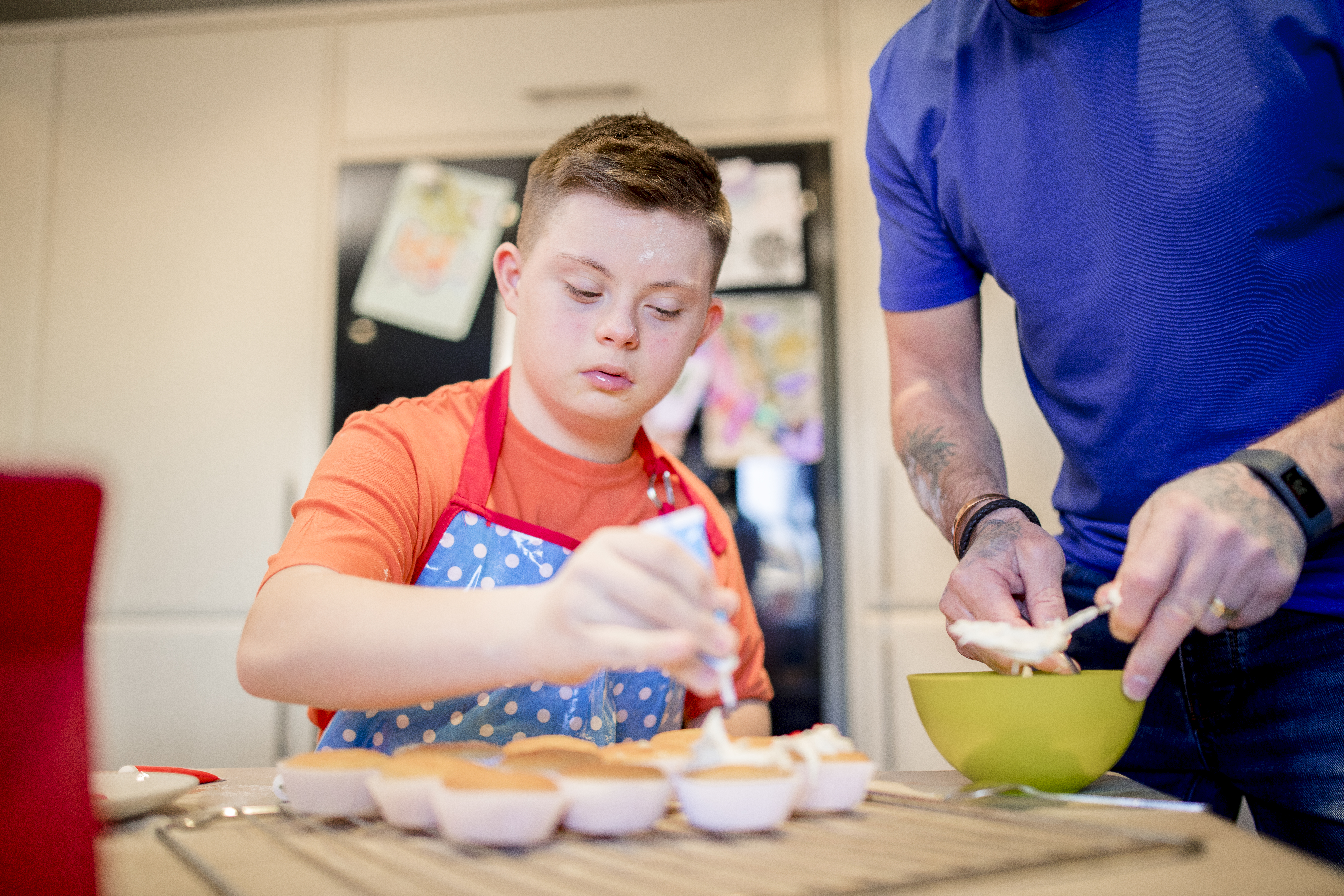 A boy with down syndrome bakes cakes with his father in the kitchen.