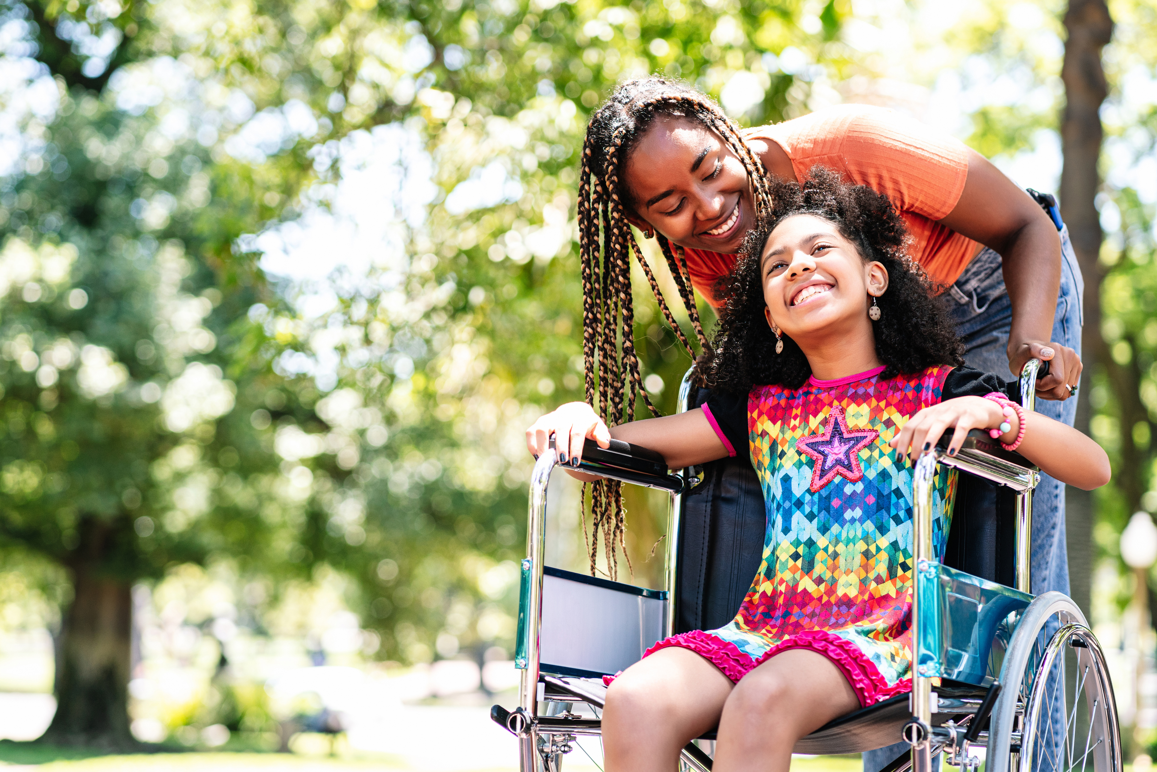 A little girl in a wheelchair enjoying a walk at the park with her mother.