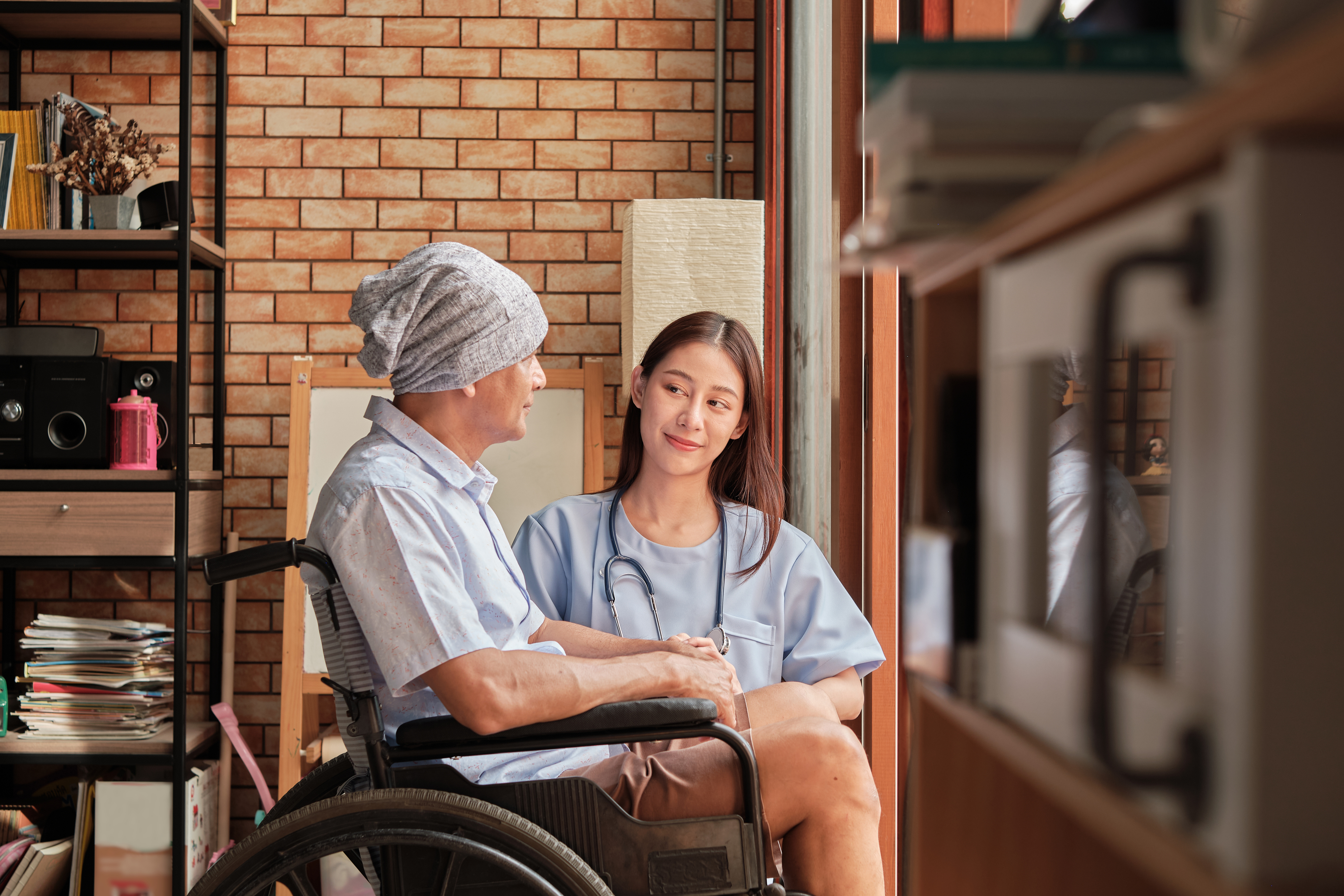 Cancer elderly patients in wheelchairs receive rehabilitation treatment in private home, Asian female doctor medical therapy treatments by talking to cure loneliness and encourage them with a smile.