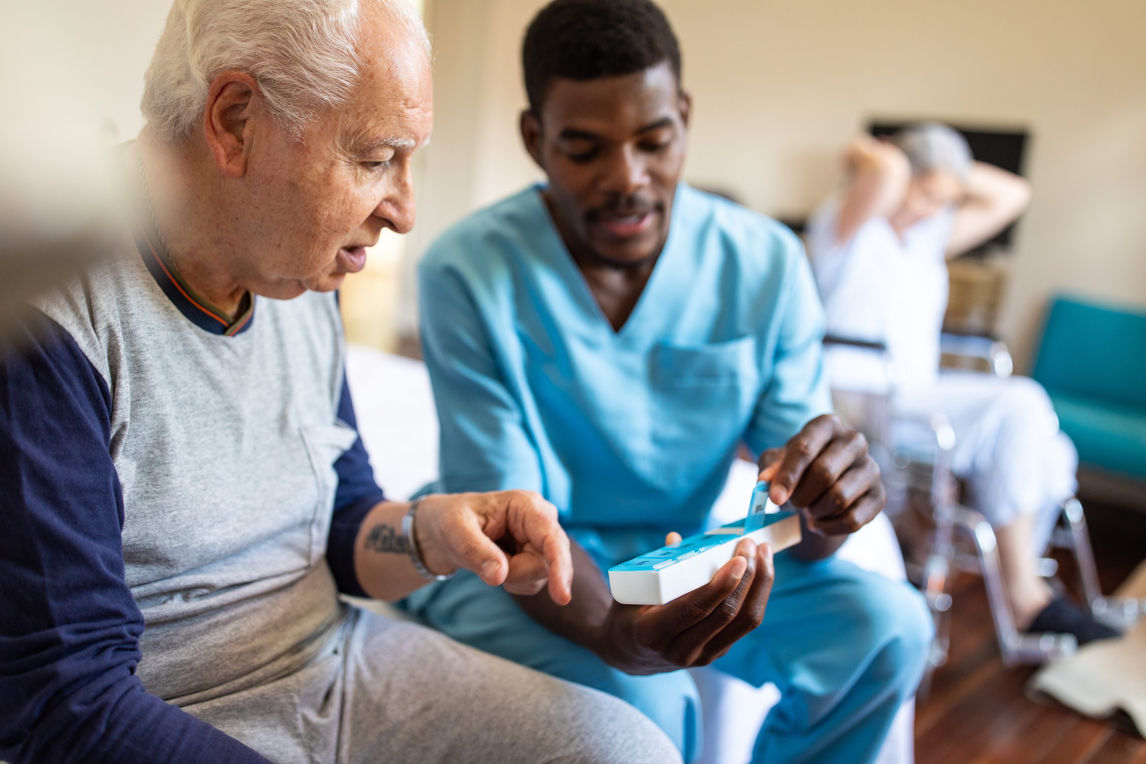 Black male nurse giving instructions to senior patient when to take his pills Black male nurse sitting on bed and giving instructions to senior patient when to take his pills in nursing home