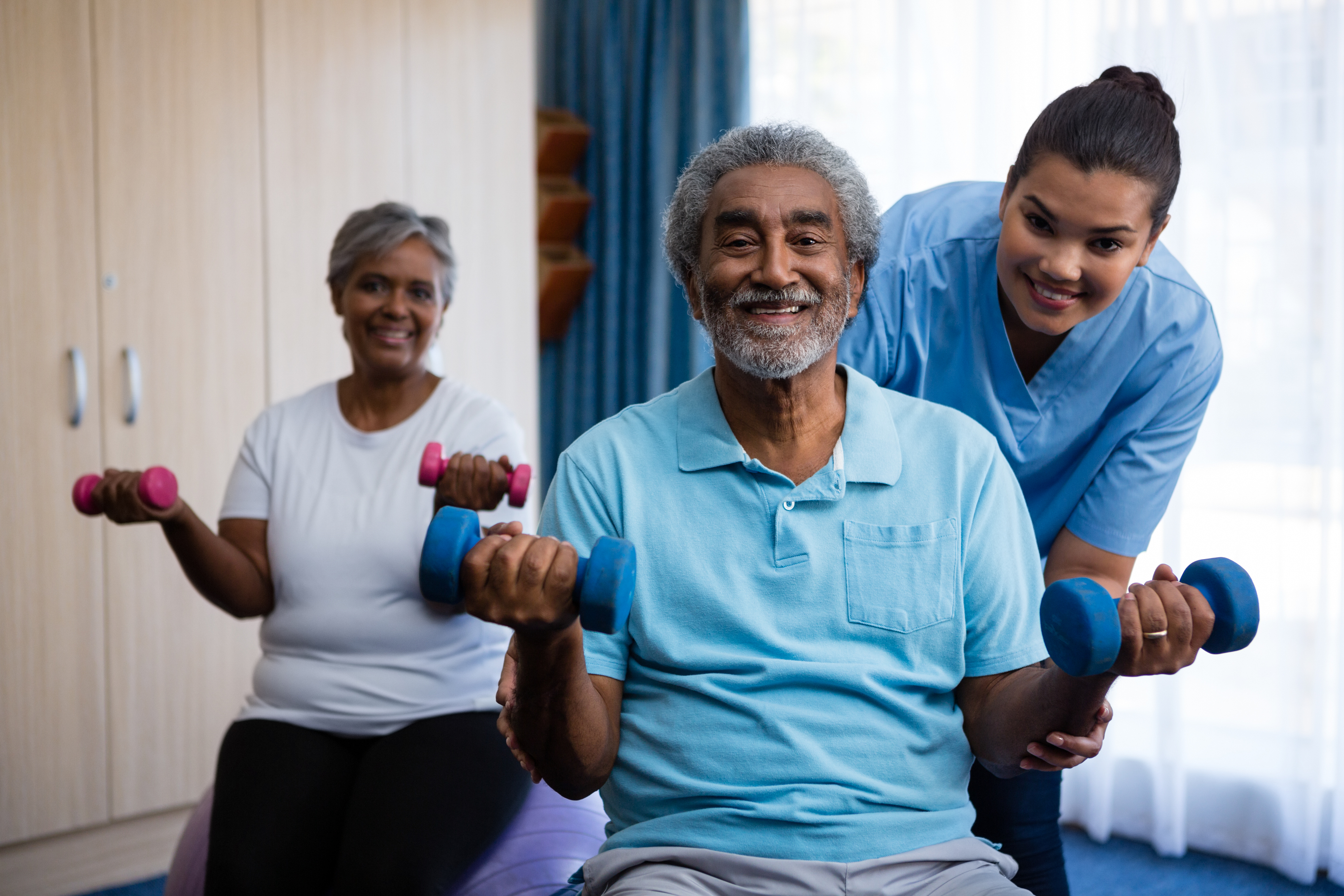 Portrait of nurse training seniors in lifting dumbbells at nursing home