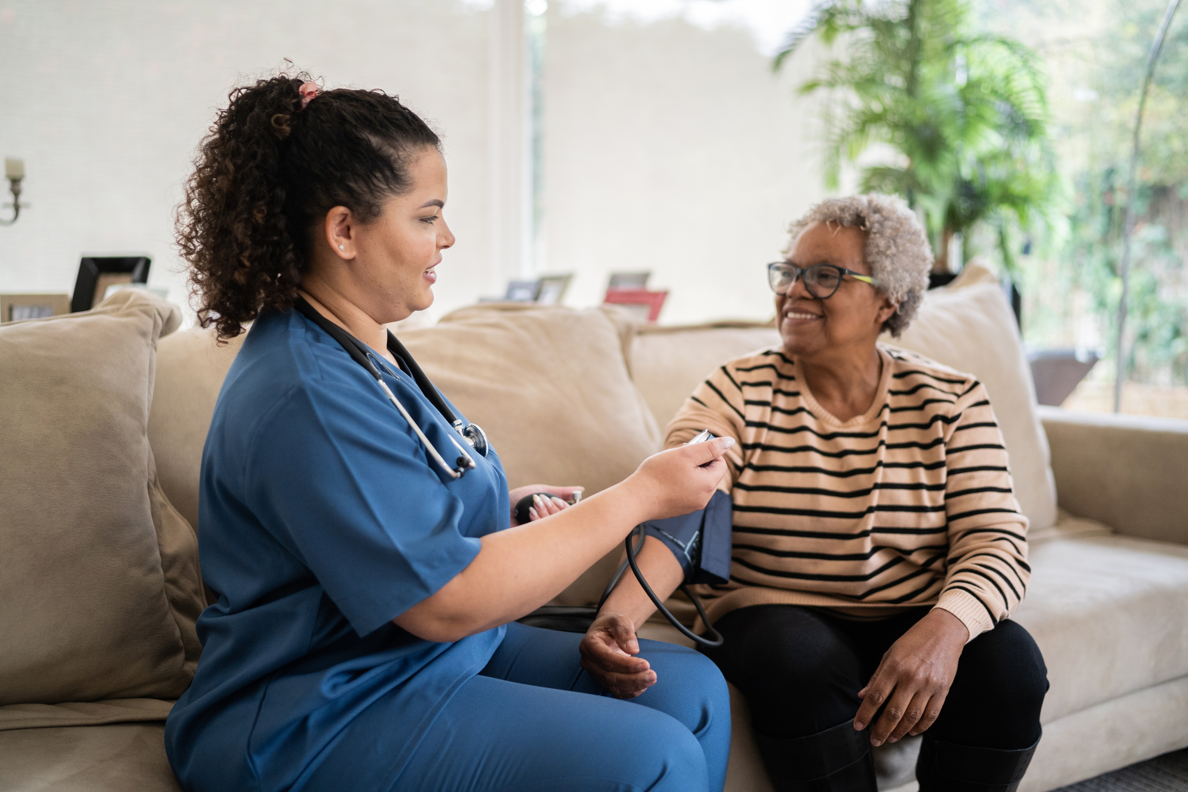 Healthcare worker taking blood pressure of senior woman at home