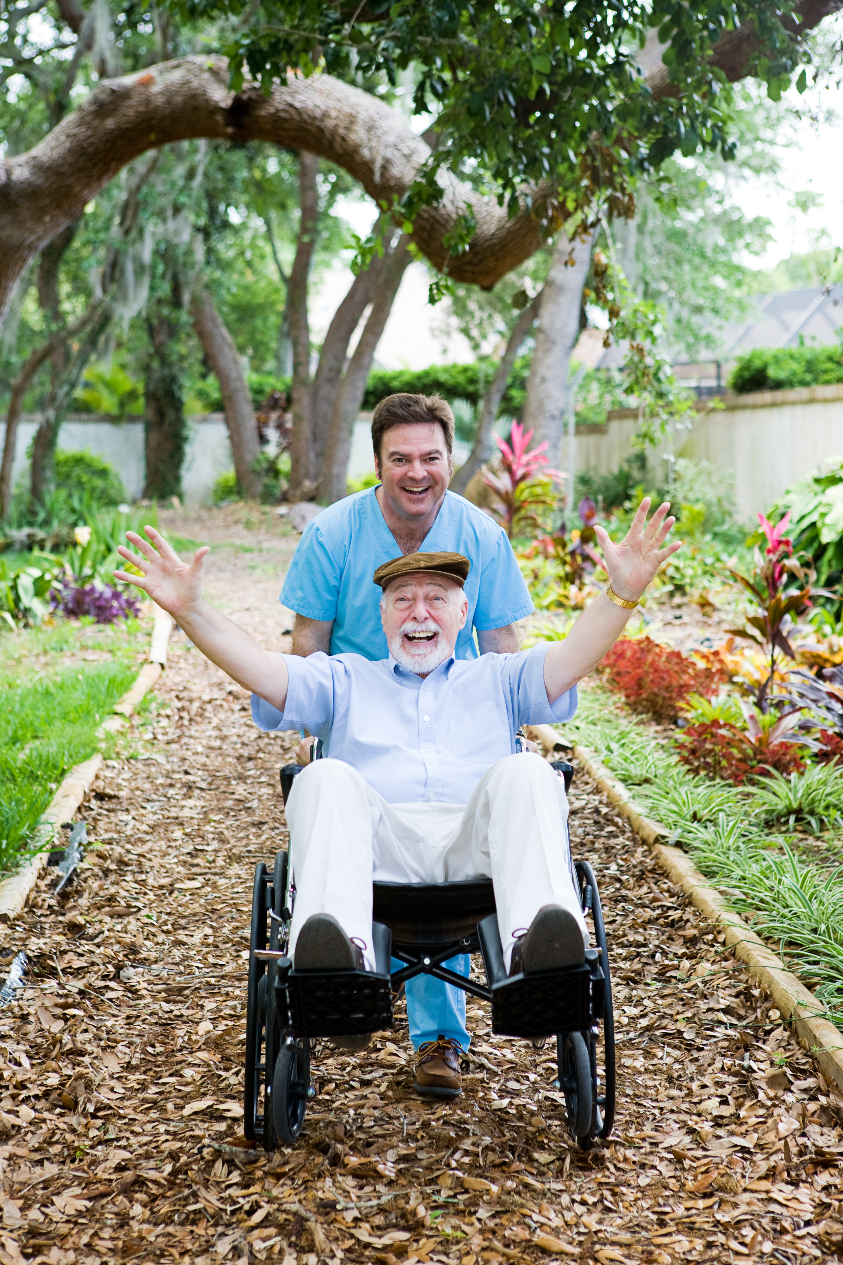 Caring nursing home orderly pops a wheelie with an elderly man's wheelchair.  They are having fun.