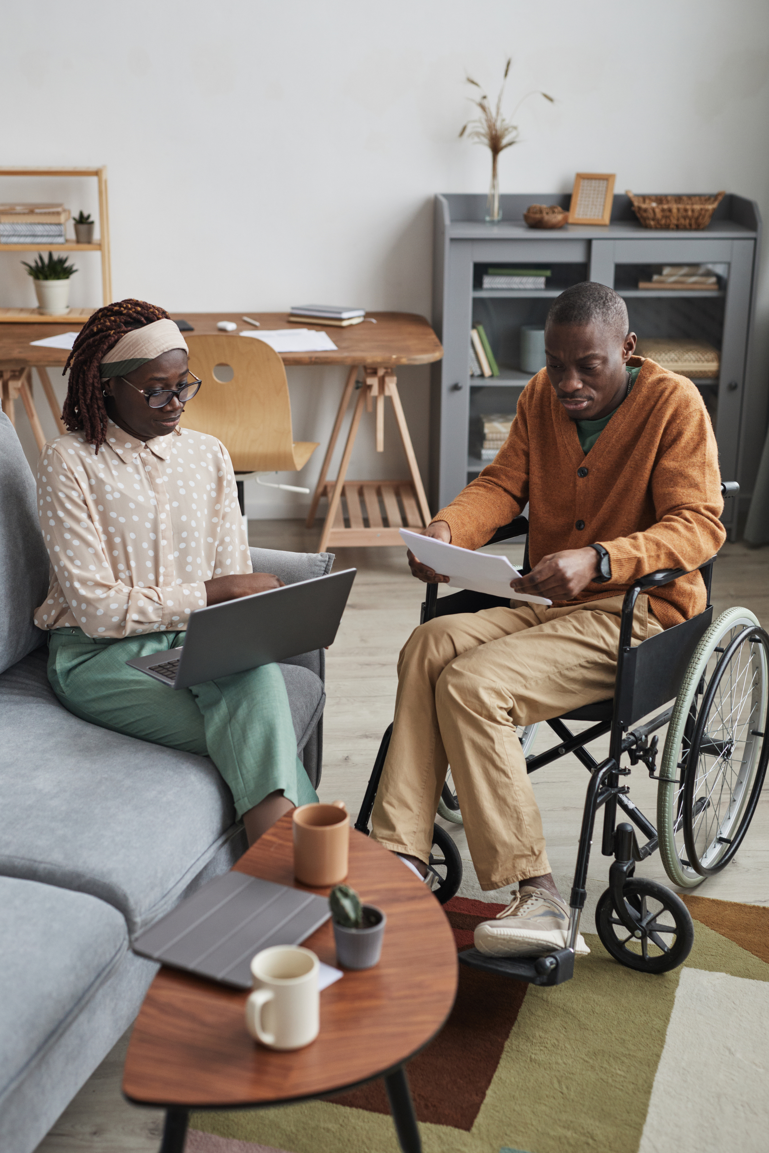 Vertical full length portrait of African-American couple with handicapped man working from home together in modern interior